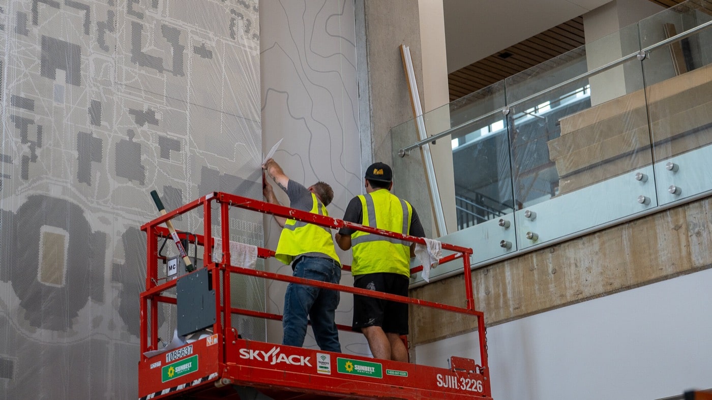 Installers on a scissor lift hanging a large wall graphic
